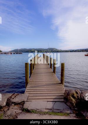 Vue panoramique sur la jetée en bois s'étendant dans les eaux calmes du lac Windermere sous un ciel spectaculaire. Le lac tranquille, collines environnantes. Banque D'Images