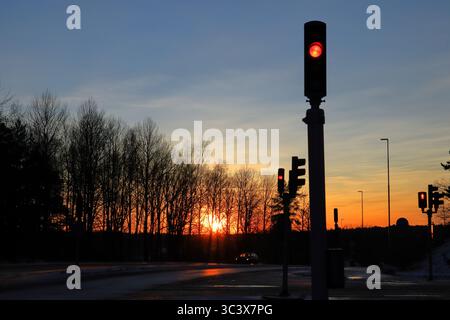 Coucher de soleil avec feux tricolores. Silhouettes sombres. Heure dorée avec un soleil rouge. Panneau stop sous-exposé. Belle image. Stockholm, Suède, Europe. Banque D'Images