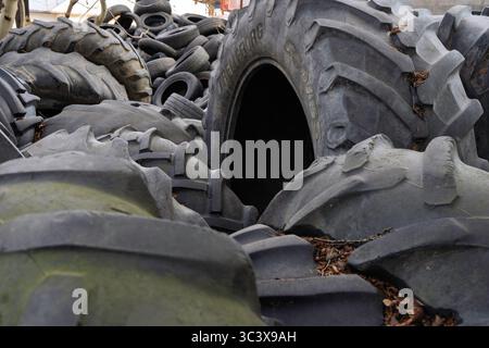 Gros tas de pneus automobiles et agricoles usagés dans un parc à la casse, prêts pour le recyclage, mettant en évidence les préoccupations environnementales en matière de déchets. Banque D'Images