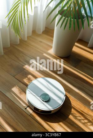 Aspirateur robot blanc sur plancher en bois. Technologie de nettoyage intelligente Banque D'Images
