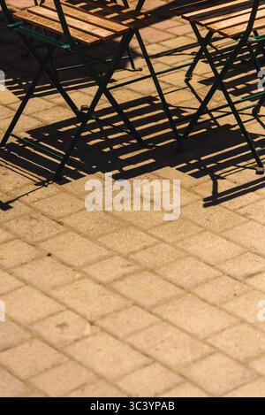 Ombres de métal vide et chaises en bois projetées sur un pavé ensoleillé dans un cadre de café en plein air. Mise au point sélective. Banque D'Images