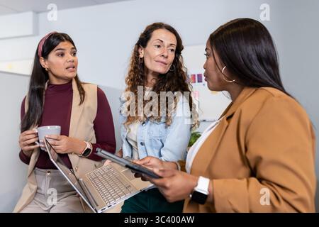 Diverses collègues féminines se réunissant dans un espace de travail lumineux avec des notes adhésives pour tablette portable Banque D'Images