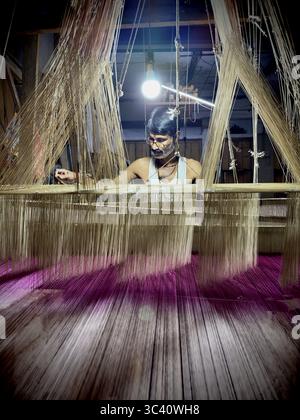 Un homme tisse des tissus de soie pour saris sur un métier à tisser antique. Le sari se compose d'un tissu sans couture d'environ 1,20 mètres de large et d'environ 6 mètres de long. Trad Banque D'Images