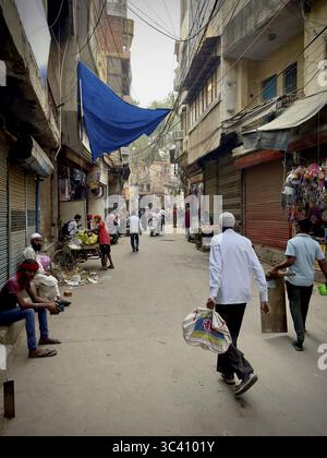 Les gens marchant à travers une ruelle étroite dans un environnement urbain quotidien, Mehrauli, district de South Delhi, Inde Banque D'Images