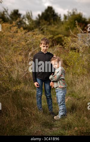 Frère et soeur debout près l'un de l'autre dans un pré herbeux. Banque D'Images