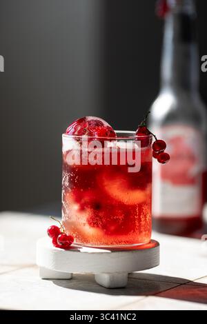 Limonade de baies dans un verre avec des sphères de glace avec des baies de cassis rouges congelées Banque D'Images