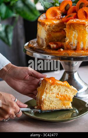 Gros plan d'une délicieuse tranche de gâteau à l'abricot servie dans une assiette verte. Le gâteau est moelleux et moelleux, fourré et garni de frais Banque D'Images