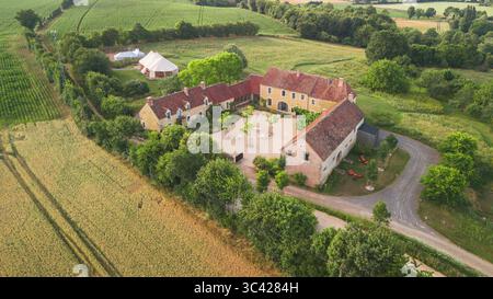 Vue aérienne d'un bâtiment majestueux avec une grande cour, bordé de verdure luxuriante et de champs dorés, baigné de chaleur de soleil, le Val Gaudry, Normandie, France. Banque D'Images