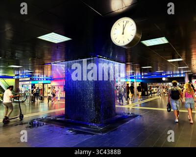 Zurich, Suisse – juillet 2025 : les gens passent devant la fontaine intérieure et l'horloge dans le passage souterrain de Zurich Hauptbahnhof. Scène de rue éditoriale. Banque D'Images