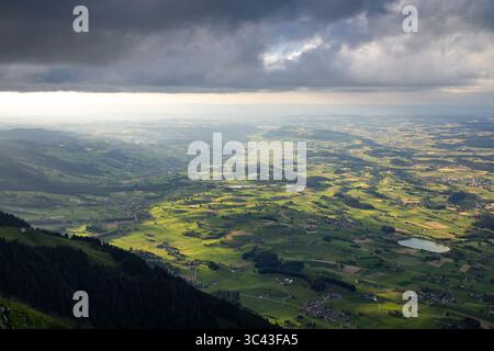 Une vue aérienne panoramique capture une vallée luxuriante et verdoyante creusée par le fleuve Aar en Suisse. Des nuages sombres et dramatiques se dessinent au-dessus de nous, partiellement illuminés Banque D'Images