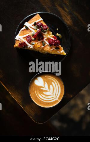 Une tranche de gâteau servie avec une tasse de cappuccino orné de latte art, placée sur une table rustique en bois. Scène de café confortable et accueillant, parfait pour un rela Banque D'Images