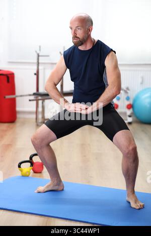 Homme faisant des exercices sur tapis bleu dans le gymnase Banque D'Images