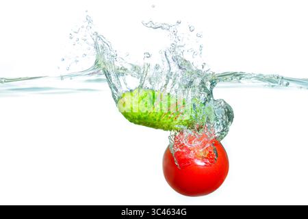 Éclaboussure vive créée par un concombre et une tomate entrant dans l'eau claire, capturant la fraîcheur et la vitalité des ingrédients sains. Banque D'Images