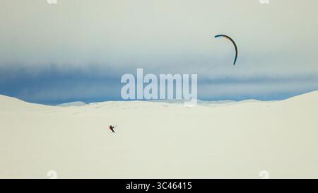 Hardangervidda, Norvège - 21 mars 2024 : une personne faisant du snowkite à travers le vaste plateau de montagne enneigé sous un ciel nuageux en Scandinavie. Banque D'Images