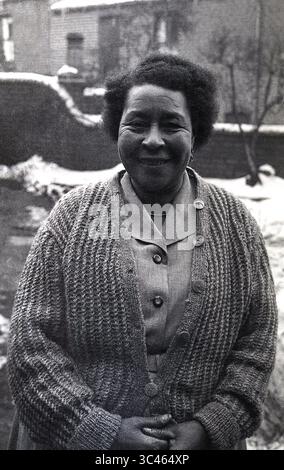 années 1950, historique, hivernal, neige sur terre et une dame mature des caraïbes debout sur un chemin à l'extérieur, souriant pour une photo. Angleterre, Royaume-Uni. Les Afro-Caribéens arrivés sur le navire à passagers, le HMT Empire Windrush en 1948, furent plus tard connus sous le nom de « génération Windrush ». Banque D'Images