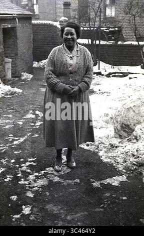 années 1950, historique, hivernal, neige sur terre et une dame mature des caraïbes debout sur un chemin à l'extérieur, souriant pour une photo. Angleterre, Royaume-Uni. Les Afro-Caribéens arrivés sur le navire à passagers, le HMT Empire Windrush en 1948, furent plus tard connus sous le nom de « génération Windrush ». Banque D'Images