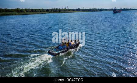 Kherson, Ukraine - 17 septembre 2021 : vue aérienne d'un robuste remorqueur naviguant sur le Dniepr, sa peinture jaune et bleue contrastant avec les eaux sombres et le littoral vert. Banque D'Images