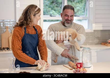 Couple pétrissant la pâte et tenant le chien Golden retriever sur le comptoir en marbre dans la cuisine Banque D'Images