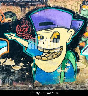 Le personnage de graffiti avec un énorme sourire et une casquette arrière illumine un mur altéré à Oaxaca, au Mexique - Street art avec attitude et flair local. Banque D'Images