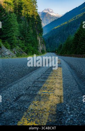 Une route sinueuse, marquée par une ligne jaune fanée, traverse le paysage luxuriant du parc national North Cascades, attirant le regard vers un m enneigé Banque D'Images