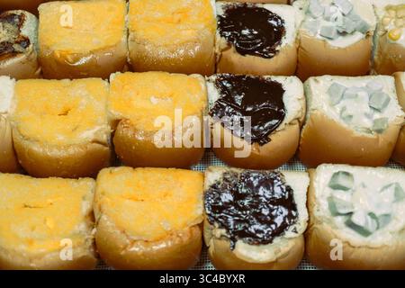 Petits pains thaïlandais fraîchement cuits à la vapeur fourrés de chocolat, beurre et crème de taro, disposés soigneusement dans un plateau. Concept de cuisine de rue nocturne avec montée de vapeur chaude. Banque D'Images
