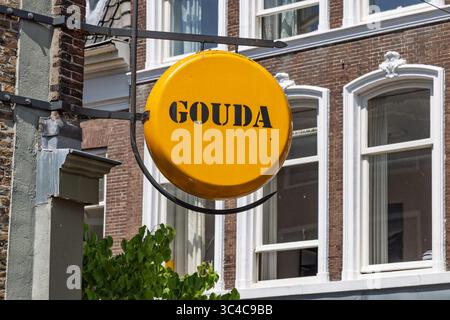 Gros plan d'un panneau rond de fromage jaune avec le mot « GOUDA » en lettres noires, accroché à la façade d'un bâtiment en briques. Gouda, pays-Bas, 29 juin Banque D'Images