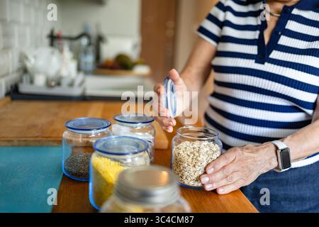 Femme âgée utilisant des bocaux en verre pour stocker de la nourriture dans la cuisine à la maison Banque D'Images