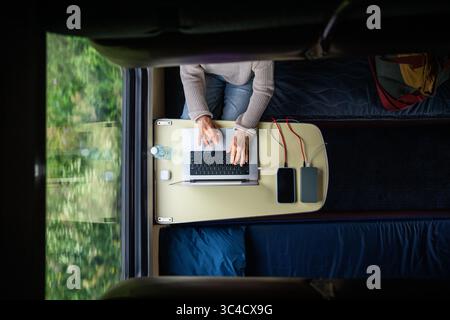Femme travaillant sur ordinateur portable tout en voyageant. Ordinateur et smartphone connectés à la banque d'alimentation, vue de dessus. Banque D'Images