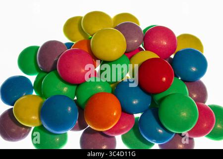 Une pile colorée de chocolats enrobés de bonbons dans diverses teintes vives, créant un arrangement vibrant et ludique sur un fond blanc Banque D'Images