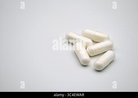 Un groupe de cinq capsules blanches opaques disposées sur un fond blanc simple, adaptées aux contextes médicaux ou liés à la santé. Banque D'Images