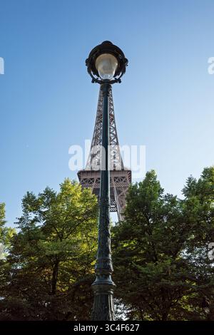 Un lampadaire orné classique se dresse haut avec la Tour Eiffel majestueusement debout derrière elle, entourée d'arbres verts sous un ciel bleu clair à Paris, Banque D'Images