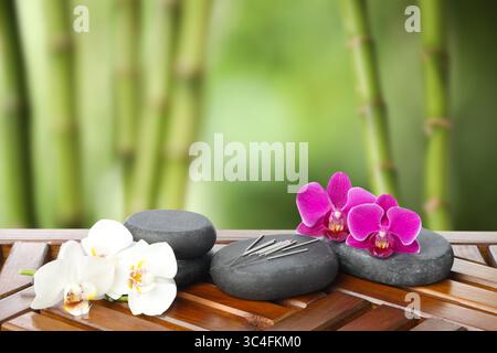 Aiguilles d'acupuncture, pierres de spa et fleurs sur table en bois à l'extérieur Banque D'Images