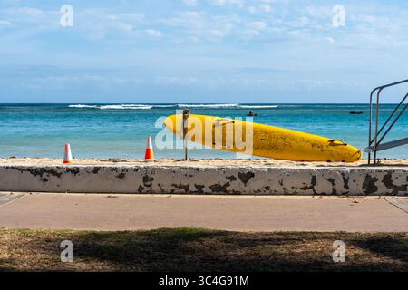 La planche de surf Yellow Lifeguard Rescue repose sur une plage tranquille, symbolisant la sécurité et la vigilance dans un ciel calme d'été avec le bord de l'océan en vue Banque D'Images