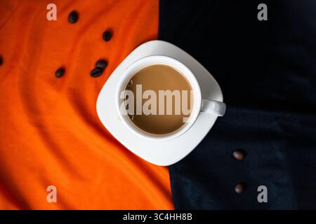 Tasse à café en céramique avec des grains de café dispersés sur fond de tissu orange et noir à double tonalité. Idéal pour la marque de café, les visuels de café, ou la nourriture audacieuse Banque D'Images