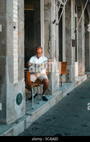Homme senior lisant le journal sur Stone Terrace dans le nord du Portugal. Architecture traditionnelle, sièges extérieurs, style de vie portugais, village européen Banque D'Images