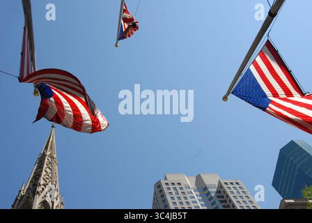 Drapeaux américains agitant contre un ciel bleu vif près de la cathédrale historique de Patrick, entourée de gratte-ciel modernes à Manhattan, New York CIT Banque D'Images