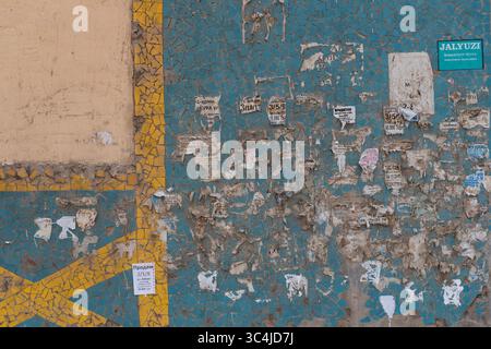 Mur urbain sale recouvert d'affiches déchirées, de vieilles publicités et de carreaux de mosaïque cassés. Pollution visuelle et concept de décomposition de la ville Banque D'Images