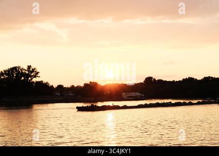 Coucher de soleil serein sur la rivière Sava à Belgrade, Serbie, avec des tons oranges chauds et une barge de passage sur l'eau. Banque D'Images