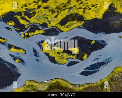 Vue aérienne des rivières glaciaires creusant des chemins à travers des sables volcaniques noirs, contrastés par des champs de mousse verte vibrants, Islande. Banque D'Images