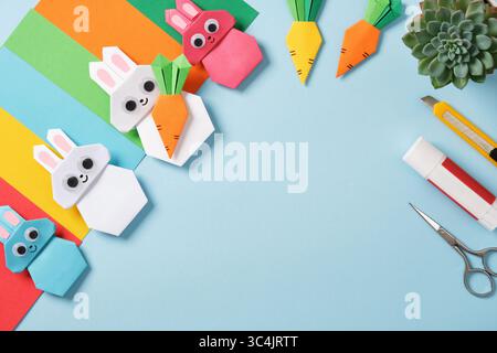 Cadre fait d'outils d'artisanat en papier : ciseaux, couteau, colle et papier coloré. Lapins et carottes origami. Concept de bricolage, travaux d'aiguille. Calque plat, copie s Banque D'Images