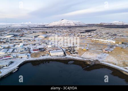 Vue aérienne du paysage monochrome évacué de Grindavik, où les eaux sombres rencontrent les bâtiments poussiéreux de neige sous un ciel pâle, contrastant avec le majesti Banque D'Images