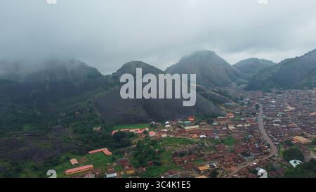 Vue aérienne des montagnes escarpées perce le ciel, projetant de longues ombres sur la ville nichée en contrebas, où les bâtiments aux toits rouges rencontrent une végétation luxuriante, Akure, Ondo, Nigeria. Banque D'Images