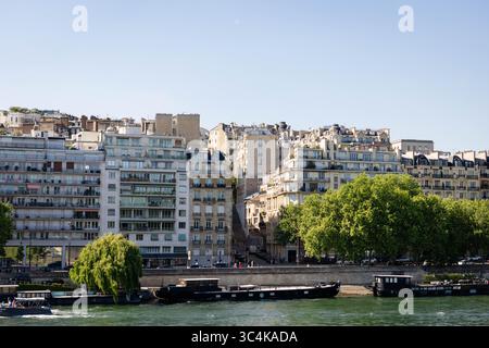 Un paysage urbain pittoresque parisien avec des immeubles d'appartements à plusieurs étages, des arbres verdoyants bordant la Seine et plusieurs péniches. Le brick Banque D'Images