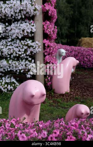 Charmante exposition de sculptures roses entourées de fleurs colorées dans un cadre de jardin luxuriant avec des pétunias roses et blancs vibrants et Banque D'Images