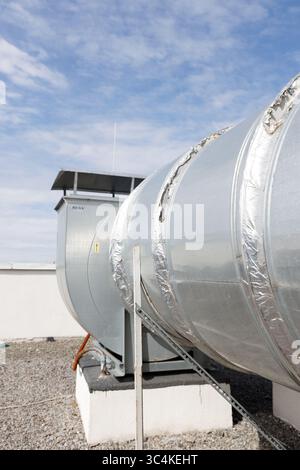 Grand système de ventilation industriel avec un conduit argenté avec isolation et une unité de contrôle, placé contre un ciel bleu lumineux avec des nuages Banque D'Images