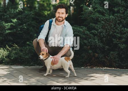 Bel homme se détendant avec son chien dans un parc urbain par une journée ensoleillée, profitant de temps de loisirs en plein air pendant l'été Banque D'Images