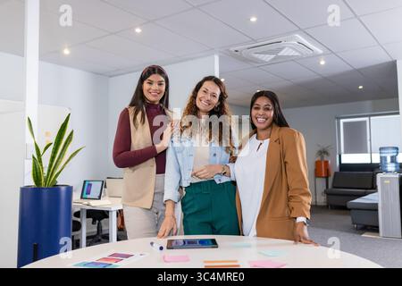 Diverses collègues féminines examinant des échantillons, des notes adhésives et une tablette autour de la table dans un bureau moderne Banque D'Images
