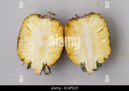 Vue de dessus d'un ananas mûr et juteux, ananas comosus, parfaitement coupé en deux et reposant sur un fond en bois. Délicieux fruits tropicaux avec y vibrant Banque D'Images