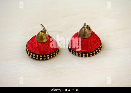 Belle paire de boucles d'oreilles anciennes Jhumka rouge pour femmes, élaborées avec du fil de soie, élégamment présentées sur un fond en bois. Banque D'Images