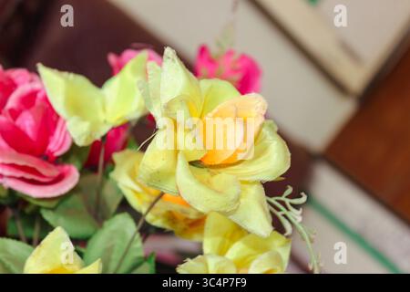 Fleurs artificielles vibrantes avec accent sur les fleurs jaunes et roses entourées de feuilles vertes Banque D'Images